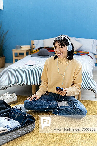 Smiling young woman with smart phone listening music in bedroom