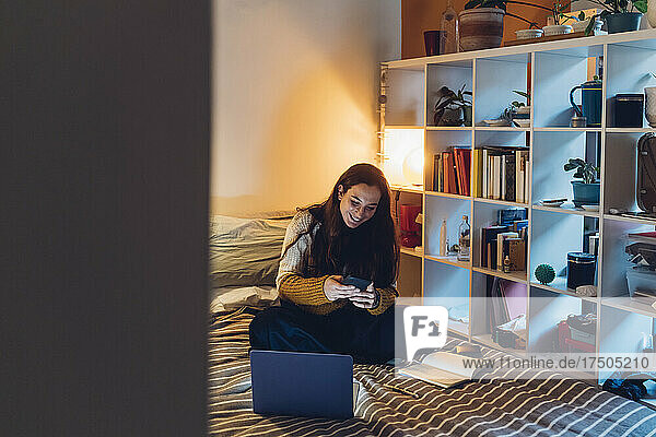 Smiling woman using smart phone by rack at home