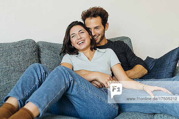 Cheerful couple sitting on sofa in living room at home