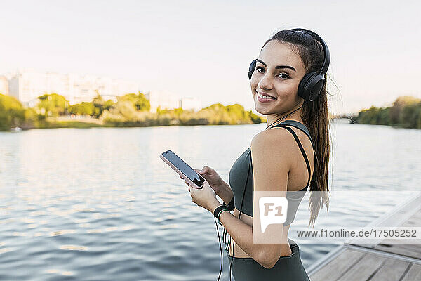 Smiling athlete holding mobile phone at river