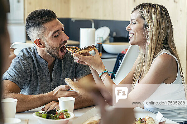 Blonde Geschäftsfrau füttert Geschäftsmann im Büro mit Pizza
