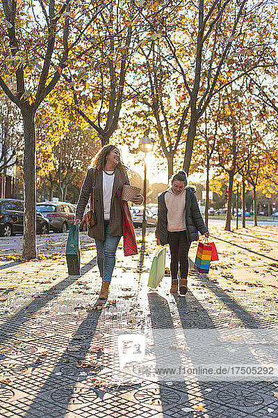 Mother and daughter with shopping bags walking on footpath in autumn