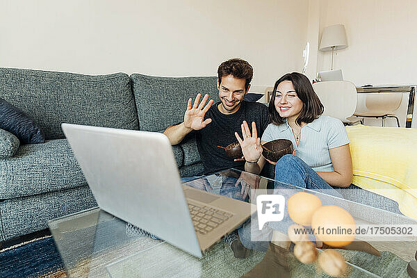 Smiling young couple waving on video call through laptop at home
