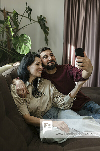 Couple taking selfie through mobile phone on sofa
