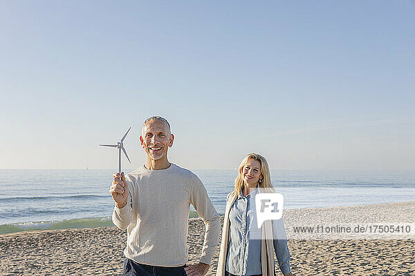 Man holding wind turbine model standing with wife at beach