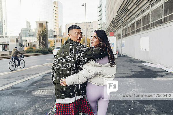 Junges Paar schaut sich beim Gehen auf dem Bürgersteig in der Stadt über die Schulter