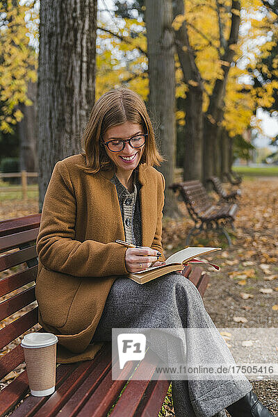 Smiling woman writing in book in autumn park