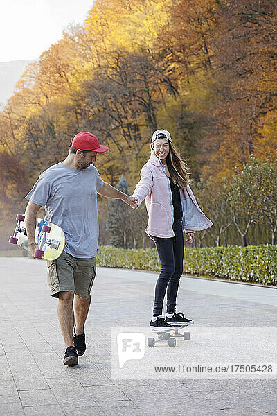 Man walking holding woman's hand skateboarding on footpath
