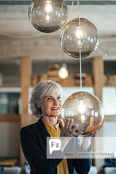 Thoughtful businesswoman holding illuminated pendant light in office