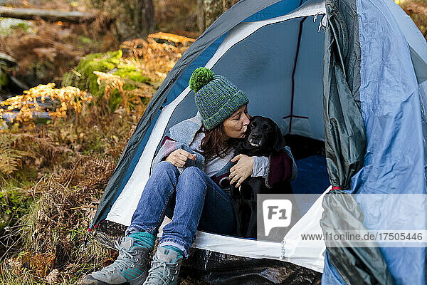 Woman kissing Labrador Retriever in tent at forest