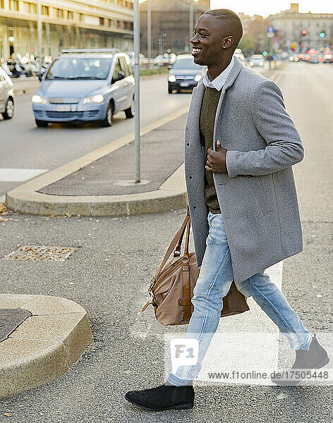 Businessman in long coat holding duffel bag walking on road in city