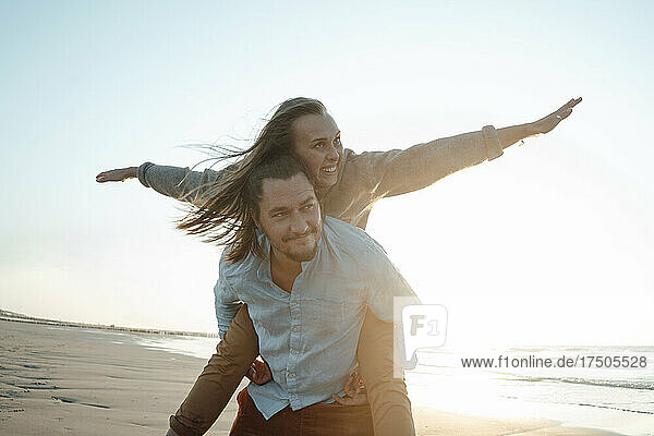 Man piggybacking carefree girlfriend at beach