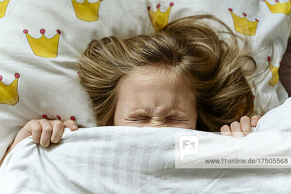 Girl grimacing underneath blanket on bed