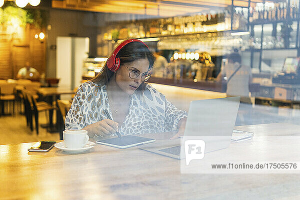 Young freelancer working on graphics tablet and laptop at cafe