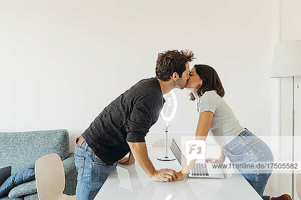 Young couple with laptop on table kissing at home