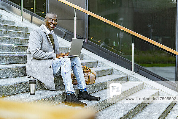 Businessman in long coat sitting with laptop on steps