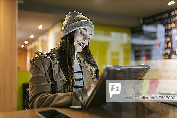 Woman using touch screen laptop at cafe seen through glass