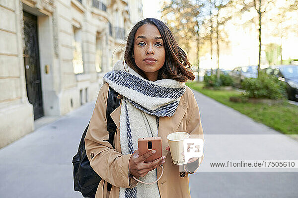 Woman holding mobile phone and coffee cup on footpath