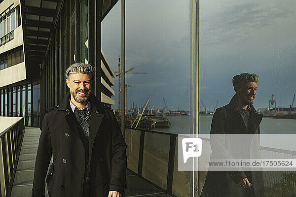 Smiling businessman walking by glass at Hafencity  Hamburg  Germany