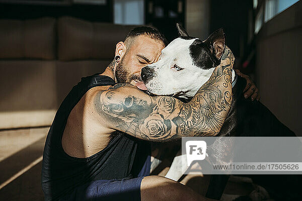 Hipster man with tattooed hand embracing dog at home