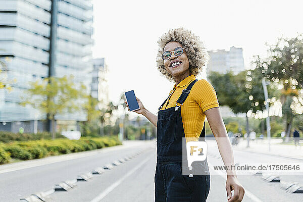 Smiling woman holding mobile phone at city street