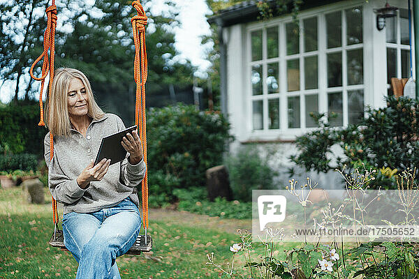 Woman using tablet PC on swing at backyard