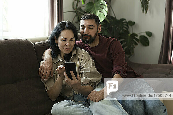 Couple using mobile phone on sofa at home