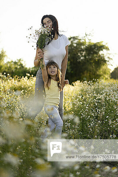 Mother smelling bunch of flowers held by daughter in meadow