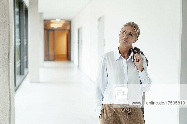 Thoughtful businesswoman with hand in pocket at office corridor