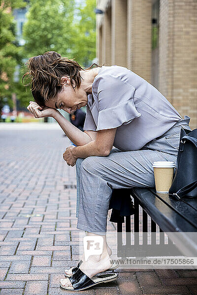 Deprimierte Geschäftsfrau mit Kopf in den Händen sitzt auf Bank am Fußweg