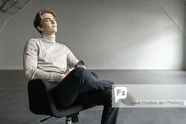 Hübscher Geschäftsmann  der auf einem Stuhl in einer leeren Industriehalle nachdenkt