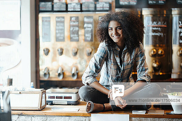 Geschäftsfrau sitzt mit gekreuzten Beinen auf der Theke einer Kaffeerösterei