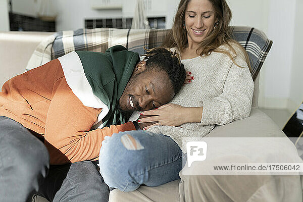 Happy man putting head on pregnant woman's belly sitting at home