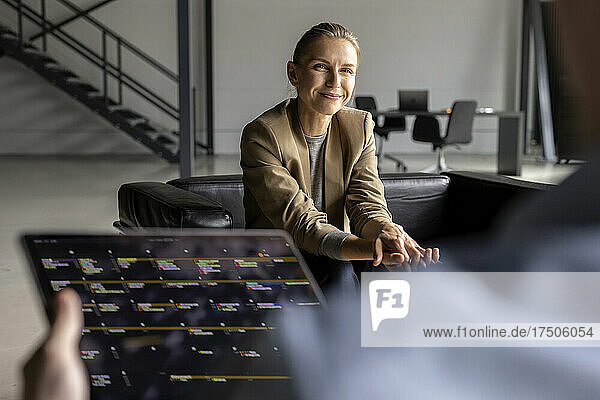 Lächelnde Geschäftsfrau blickt Kollegen mit Tablet-PC im Büro an