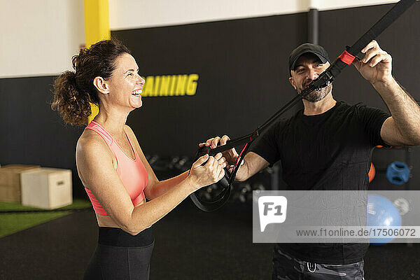 Coach adjusting straps by sportswoman in gym