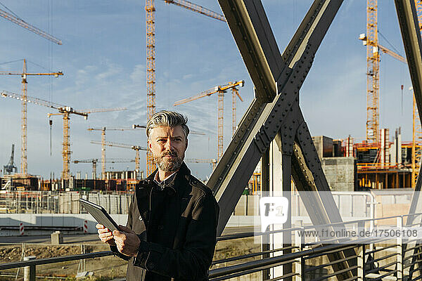 Businessman with tablet PC on bridge near construction site
