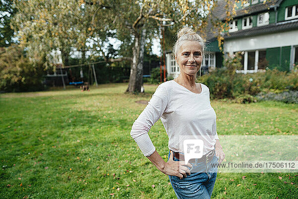 Smiling woman with hands on hip standing at backyard