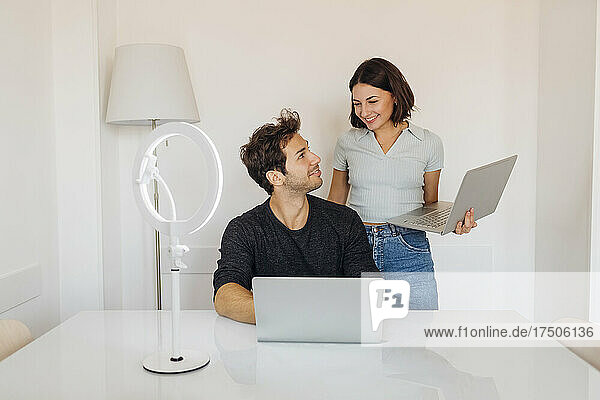 Lächelndes junges Paar mit Laptops  das sich im Homeoffice anschaut
