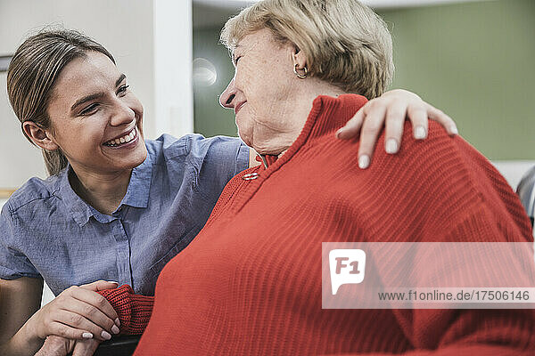 Smiling care assistant with arm around patient at home