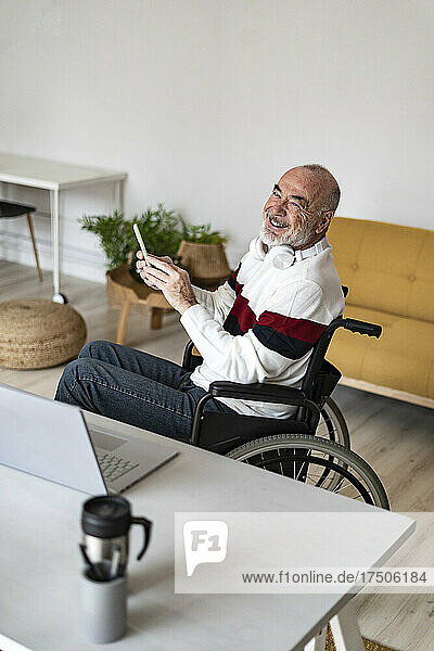 Smiling freelancer holding mobile phone on wheelchair at home office