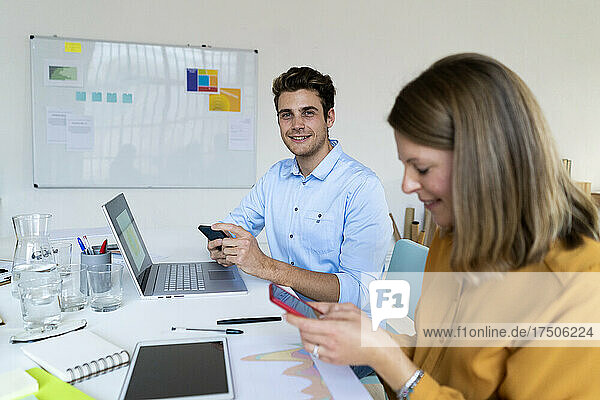 Smiling businessman holding smart phone with colleague at office