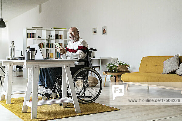 Senior disabled businessman with mobile phone and laptop at home office