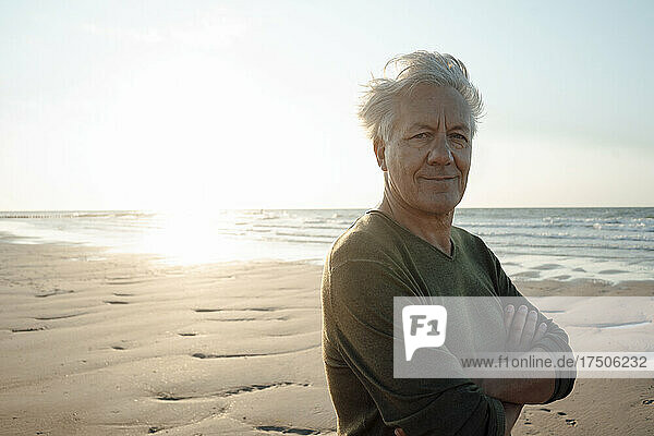 Senior man smiling with arms crossed at beach