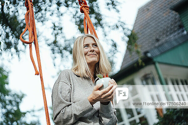 Frau hält Kaffeetasse auf Schaukel im Hinterhof