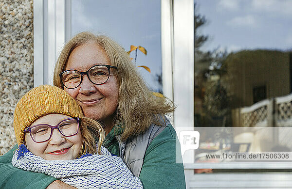 Smiling grandmother embracing granddaughter in yellow knit hat