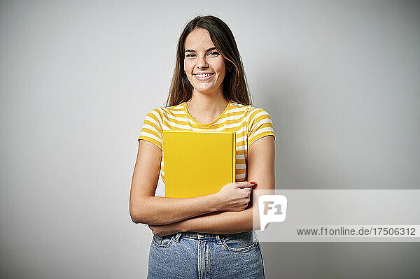 Smiling woman holding yellow book against gray background
