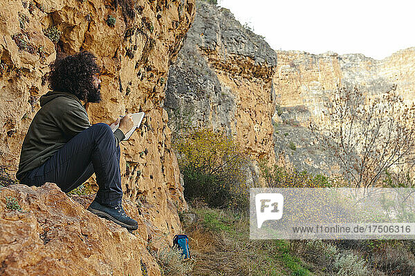 Man looking at mountain and drawing in diary