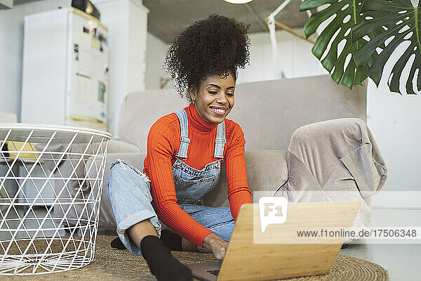 Lächelnde Frau benutzt Laptop auf Teppich im Wohnzimmer