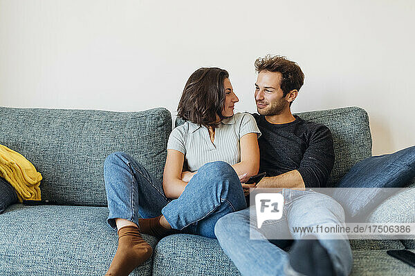 Smiling couple looking at each other while sitting on sofa