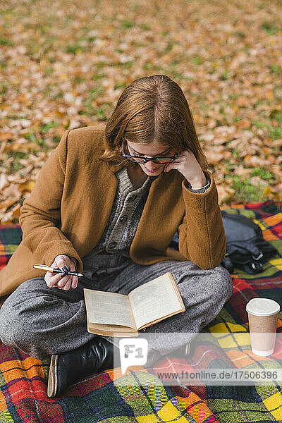 Young woman reading book in autumn park